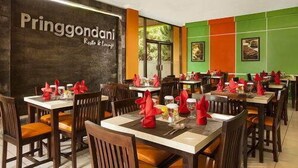A restaurant interior with multiple tables and chairs, a wall with 'Pringgondani' signage, and framed pictures on the walls. - MMUGM Hotel Yogyakarta (Depok)