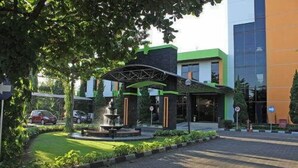 A landscaped area with a fountain, paved walkway, and a building with a green and orange facade. - MMUGM Hotel Yogyakarta (Depok)