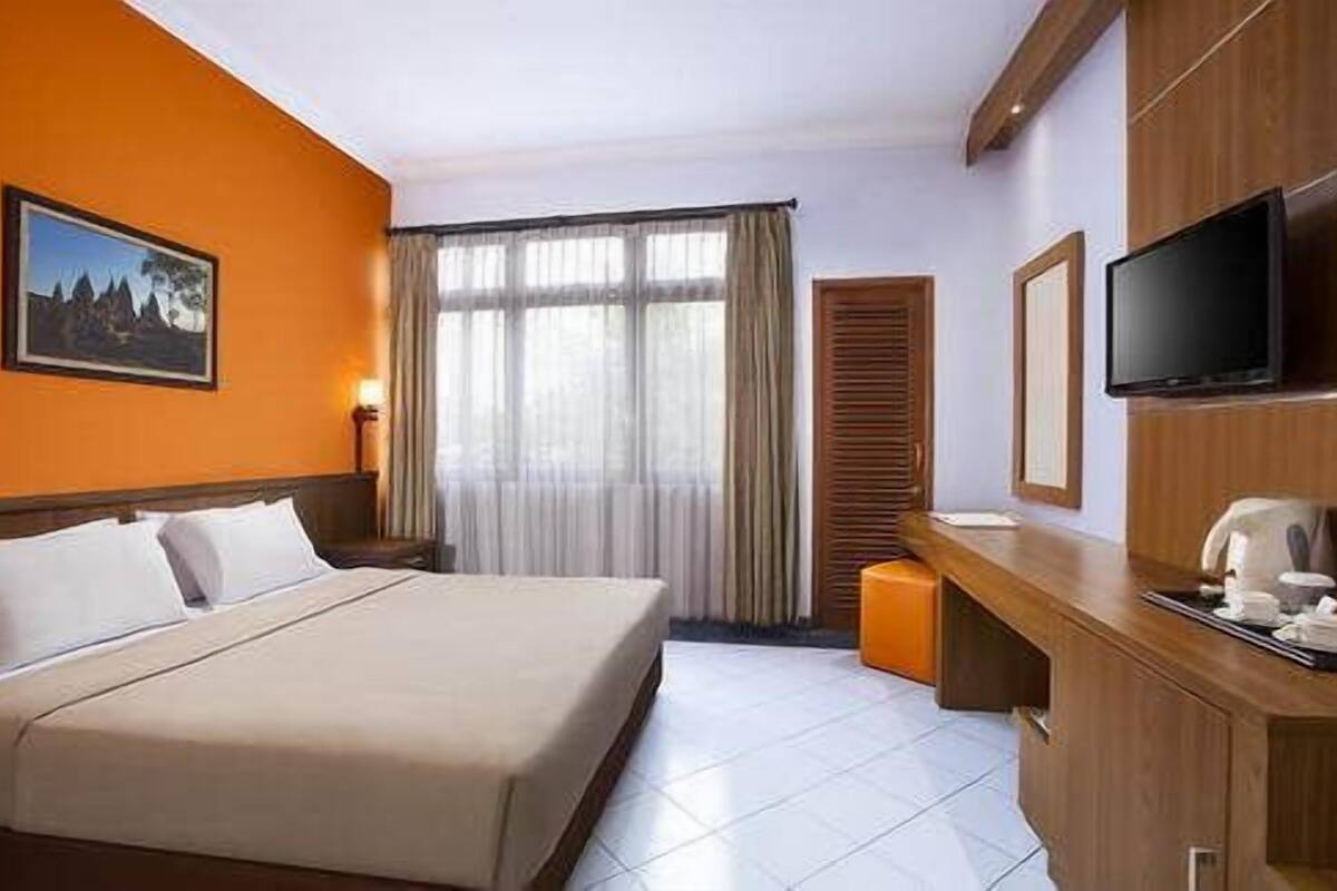 A hotel room with a bed, a desk, a television, and a window with curtains.