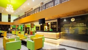 A modern reception area with a reception desk, seating area, and a balcony. - MMUGM Hotel Yogyakarta (Depok)