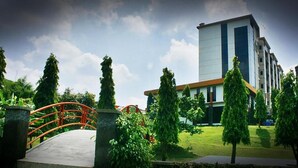A modern building with a flat roof, surrounded by greenery and a red bridge. - MMUGM Hotel Yogyakarta (Depok)