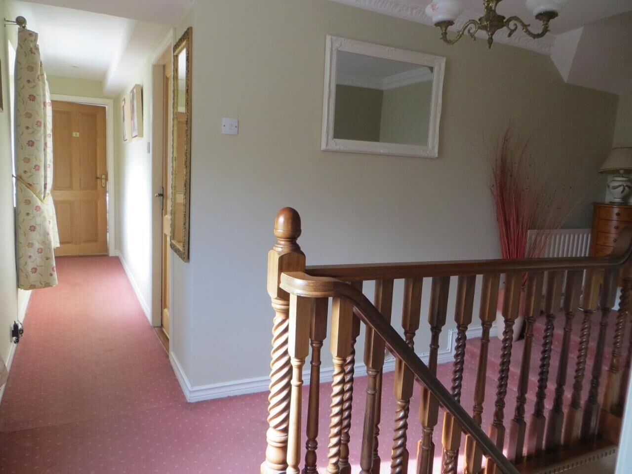 A staircase with wooden balusters and a red carpeted floor leading to a landing.