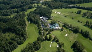 Vista aérea de um campo de golfe com um clube, rodeado por florestas densas.
