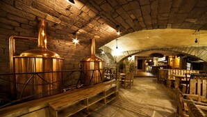 Um interior rústico com paredes de pedra, bancos de madeira e equipamentos de preparo em cobre.