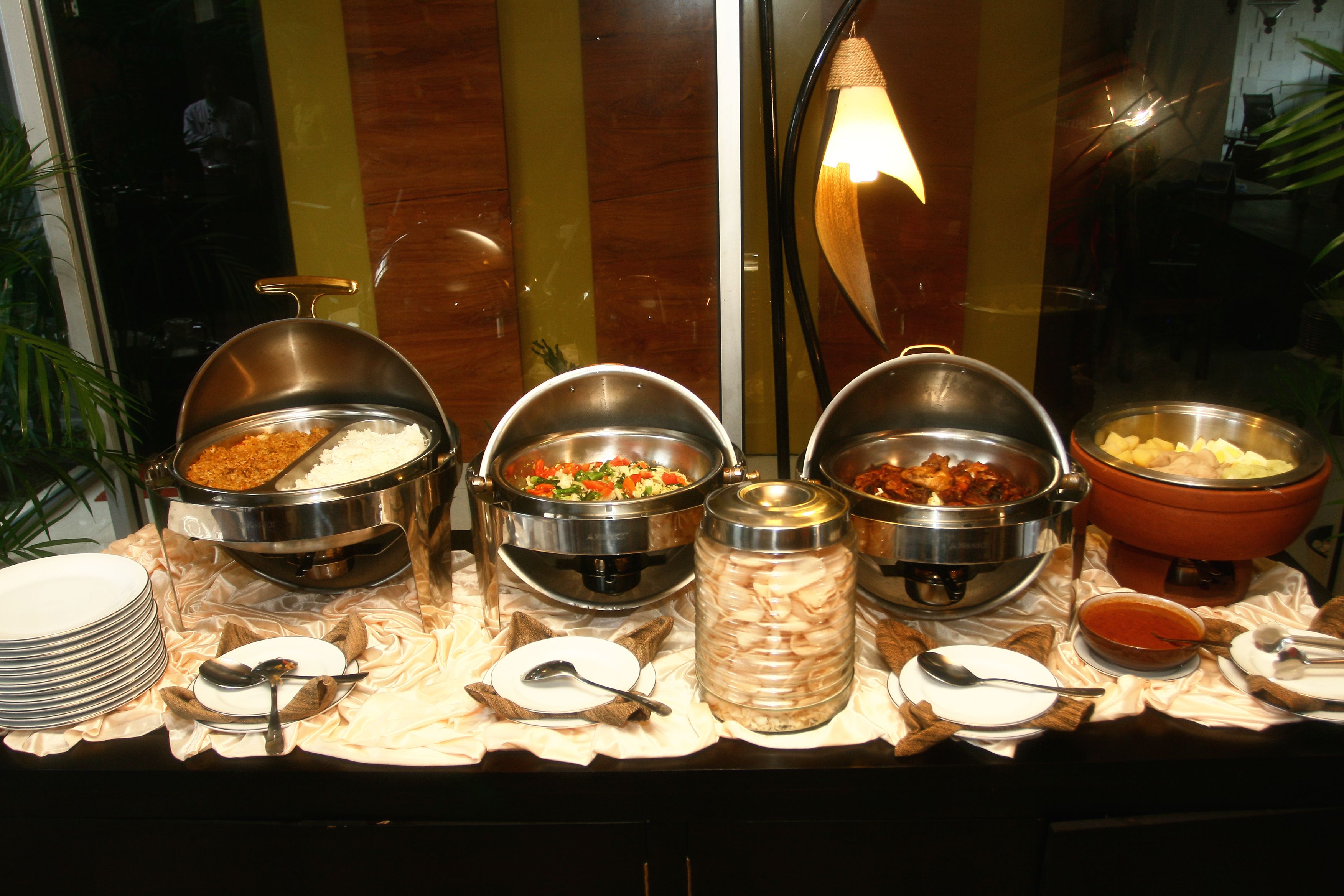 A buffet with various food items in metal containers, accompanied by plates and serving utensils.