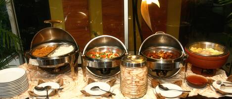 A buffet with various food items in metal containers, accompanied by plates and serving utensils.
