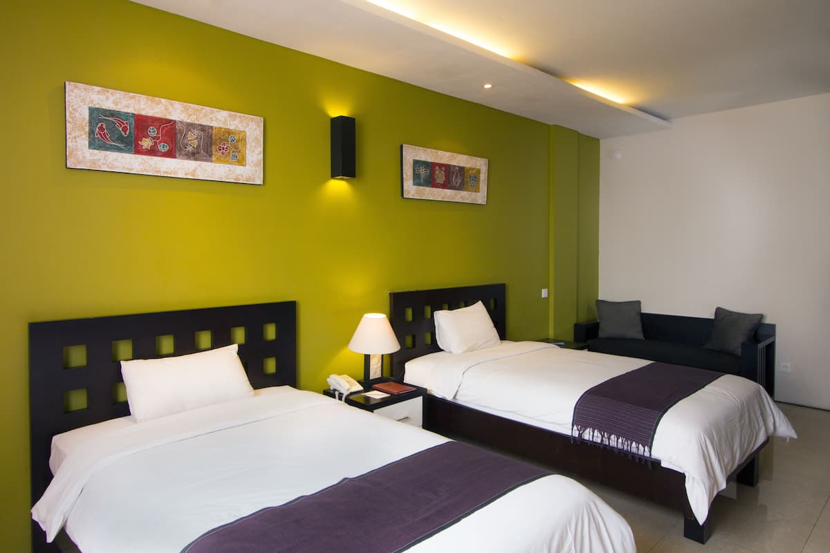 A hotel room with two beds, a nightstand with a lamp, and artwork on the walls.