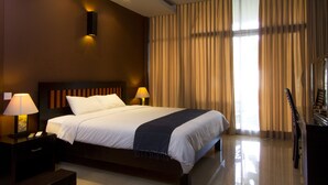 Ein Hotelzimmer mit einem großen Bett, zwei Nachttischlampen, einem Klavier und Blick ins Freie durch Vorhänge.