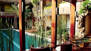 Ein Poolbereich mit Korbmöbeln, einem Glastisch und Blick auf den Pool und die umliegende Bepflanzung.