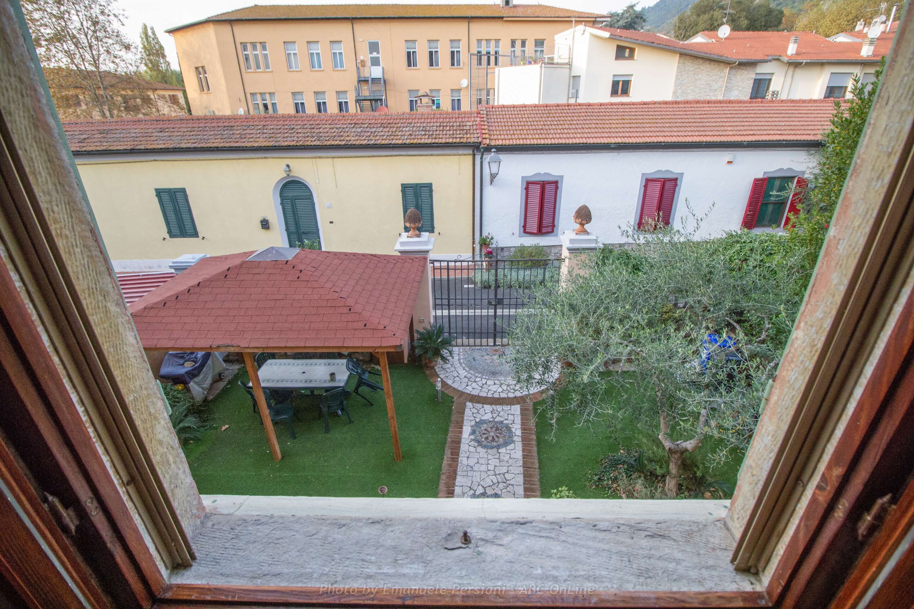 A courtyard with a red-roofed building, a white building with red shutters, and a small garden area with a table and chairs.