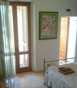 A bedroom with a bed, a window with curtains, a door, and a painting on the wall. - B&B Cribò (San Giuliano Terme)
