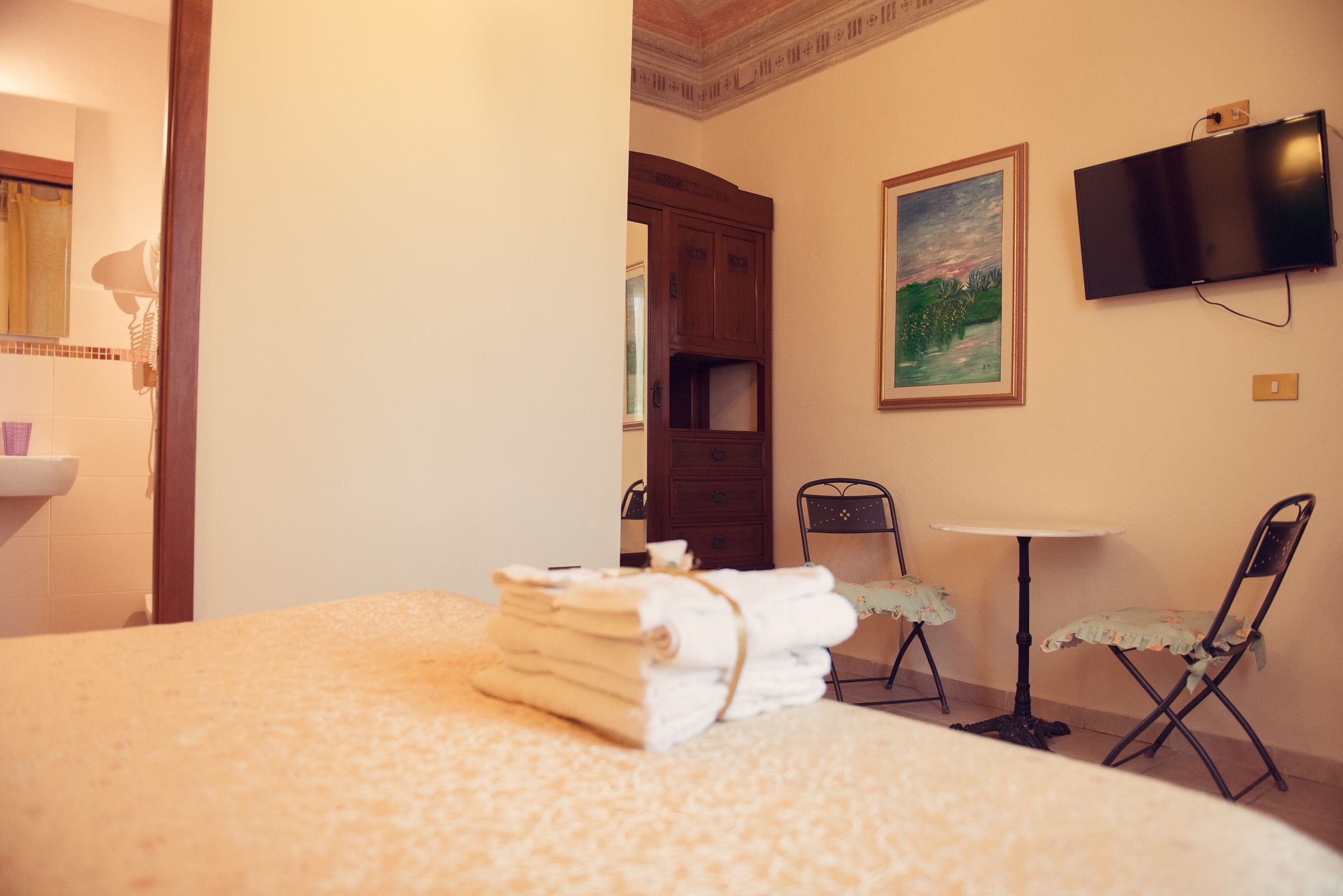 Een hotelkamer met een bed, een stoel, een klein tafeltje, een televisie en een schilderij aan de muur.