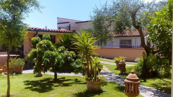 A courtyard with potted plants, a pathway, and a building with a red-tiled roof. - B&B Cribò (San Giuliano Terme)