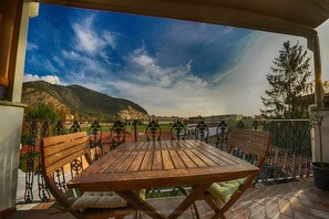 A wooden table and chairs on a balcony with a metal railing, overlooking a mountainous landscape and a body of water. - B&B Cribò (San Giuliano Terme)
