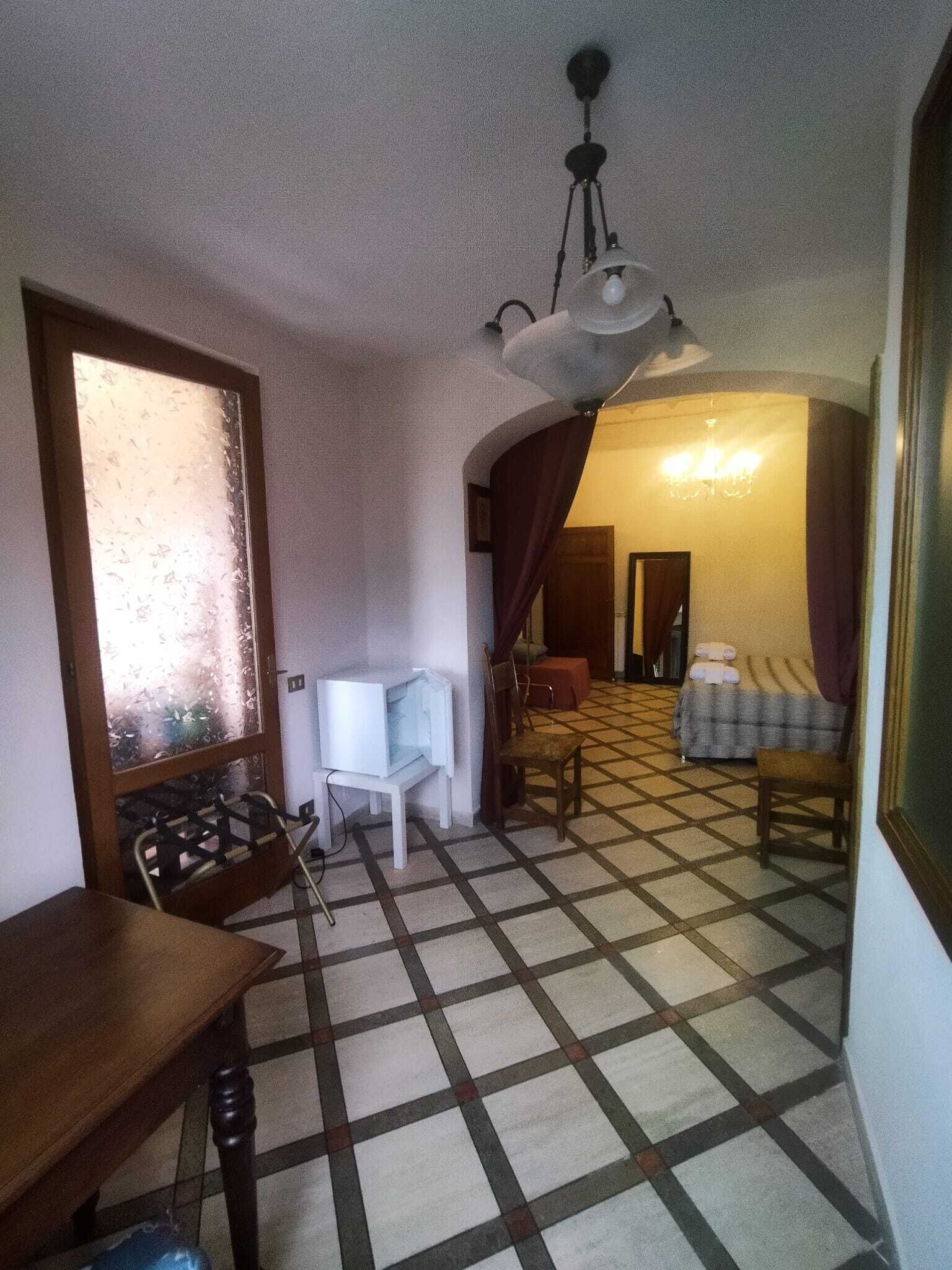 Una habitación con piso a cuadros, una mesa de madera, una silla blanca, una cama con almohadas y un candelabro.