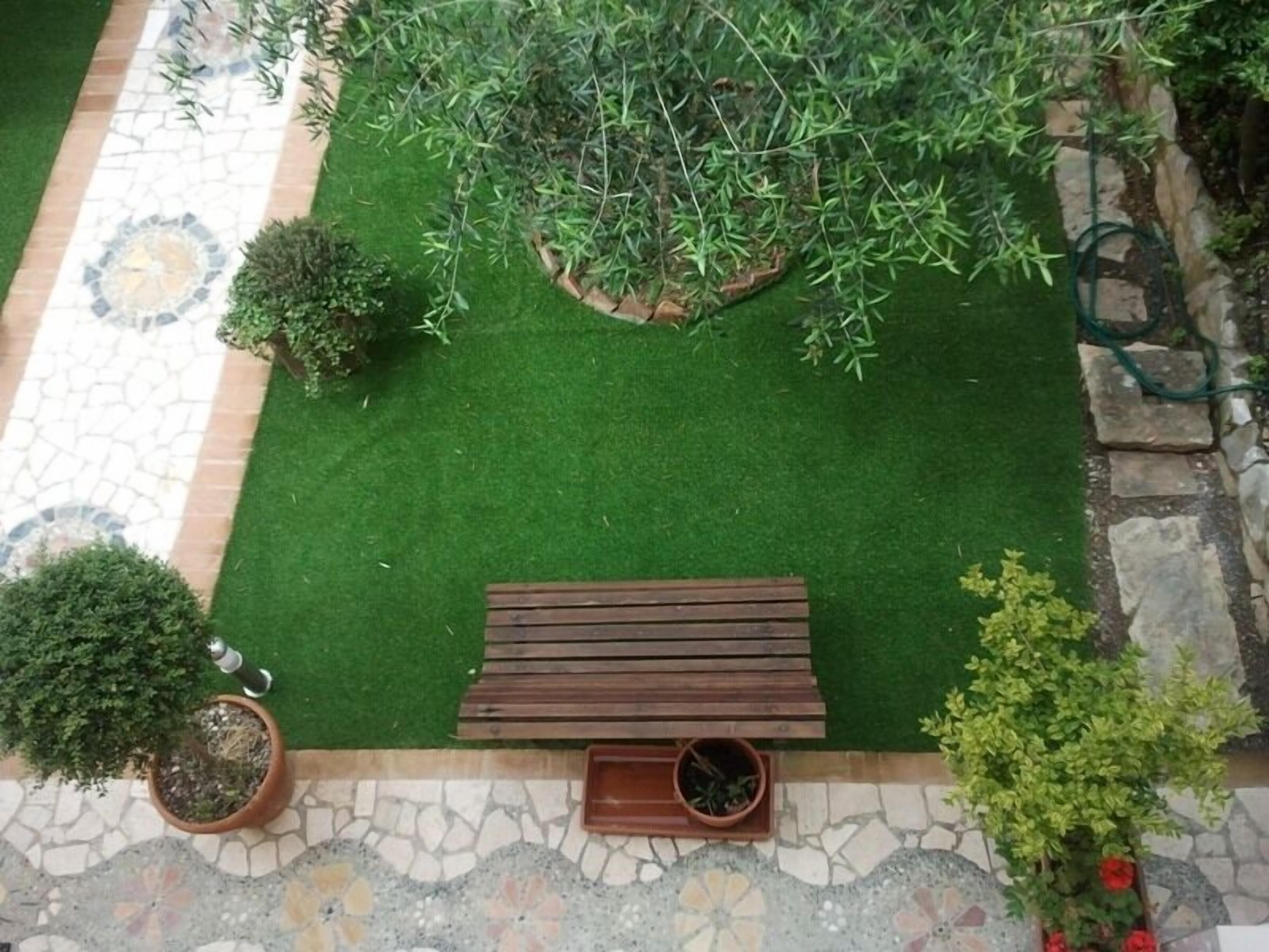 Een terras met een houten bankje, plantenpotten en een vloer van stenen tegels.