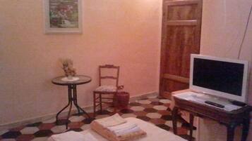 Une petite pièce comprenant un lit, une chaise, une table avec une plante, un téléviseur et une porte.