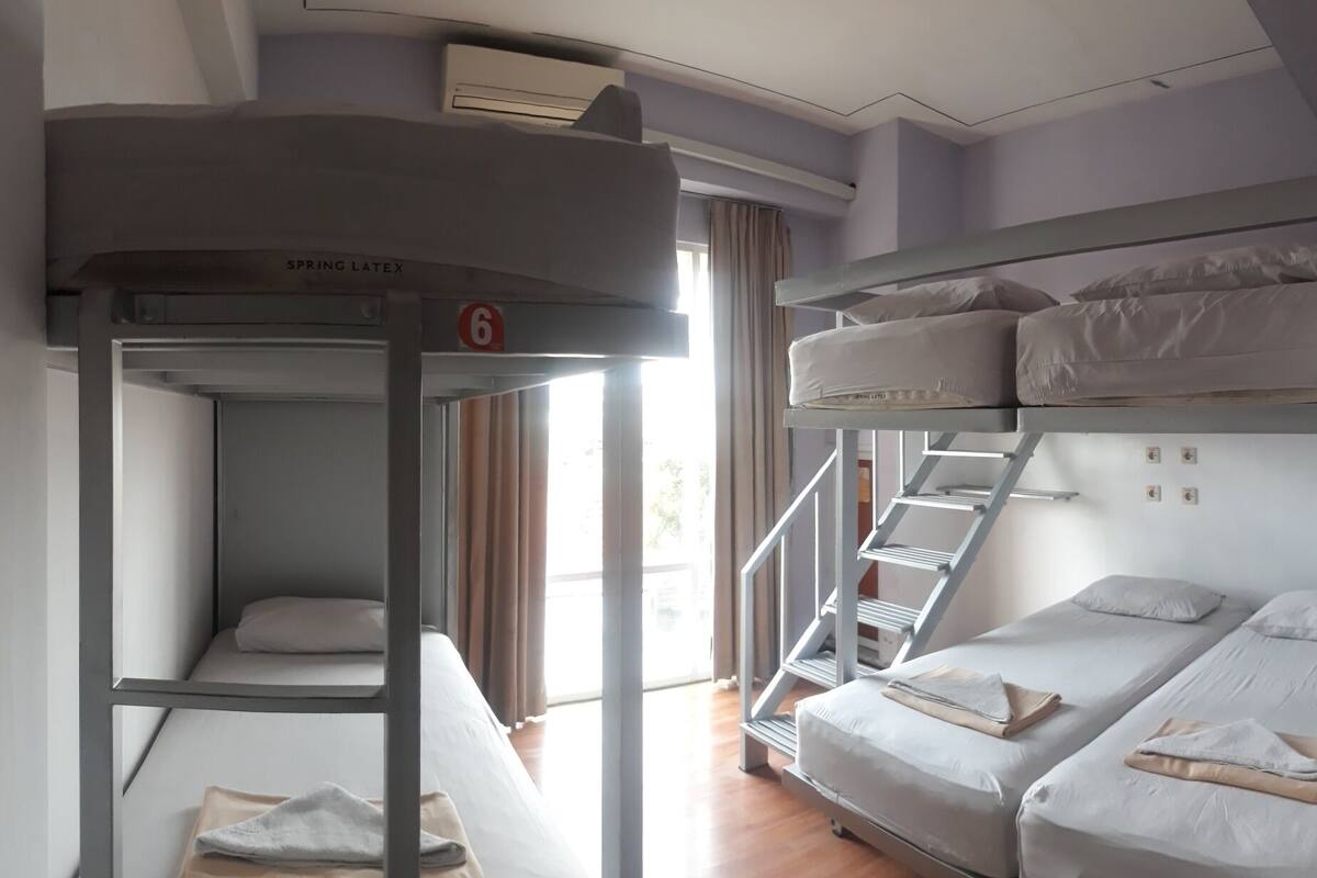 A dormitory room with bunk beds, a staircase, and a window with curtains.