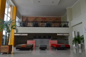 Eine Hotellobby mit einer Rezeption, drei Betten, einem Balkon und einem Wandgemälde.
