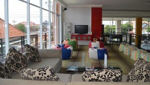 A spacious living area with a large TV, comfortable seating, and a balcony with a railing. - EDU Hostel (Yogyakarta)