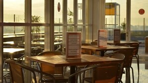 An indoor dining area with tables and chairs, large windows, and a view of the outside. - EDU Hostel (Yogyakarta)