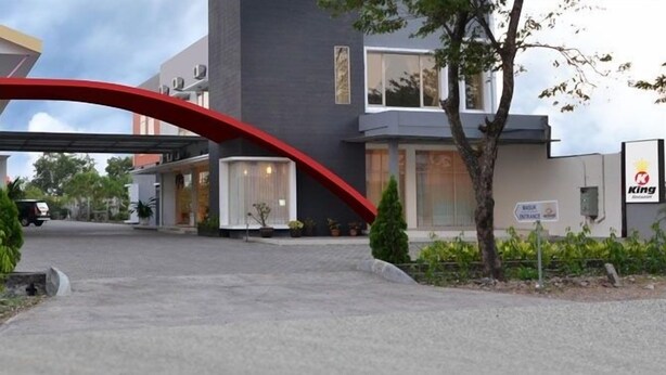 A modern building with a red archway entrance, a sign for a King restaurant, and a parking area. - Hotel Kings Kudus (Kudus)