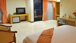 A hotel room with a bed, a desk with a television, a chair, and a balcony with curtains. - Hotel Kings Kudus (Kudus)