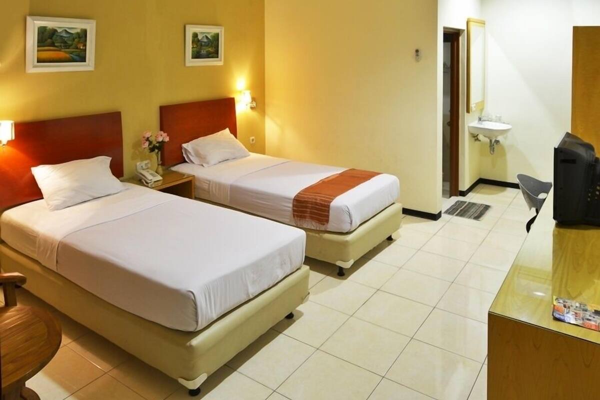 A hotel room with two single beds, a desk with a computer, a telephone, and a small table with a vase of flowers.