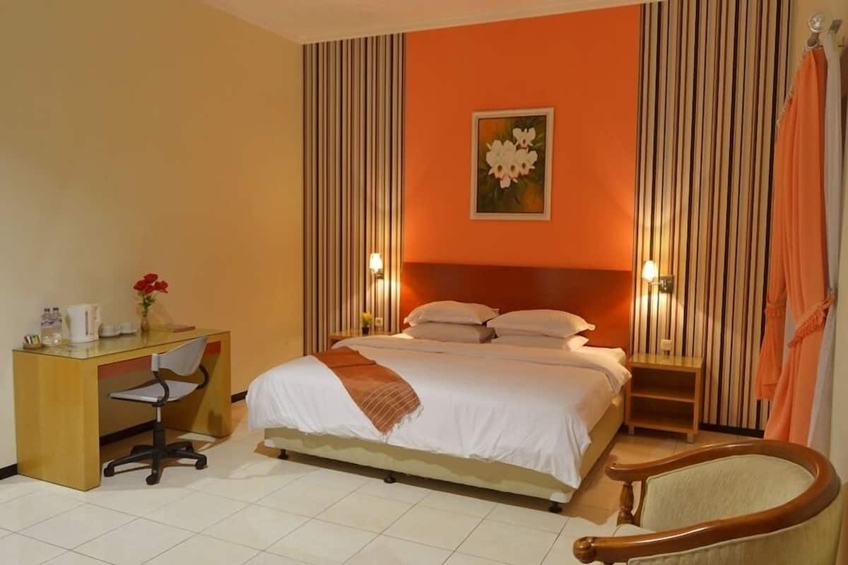 A hotel room with a bed, desk, chair, and a painting on the wall.
