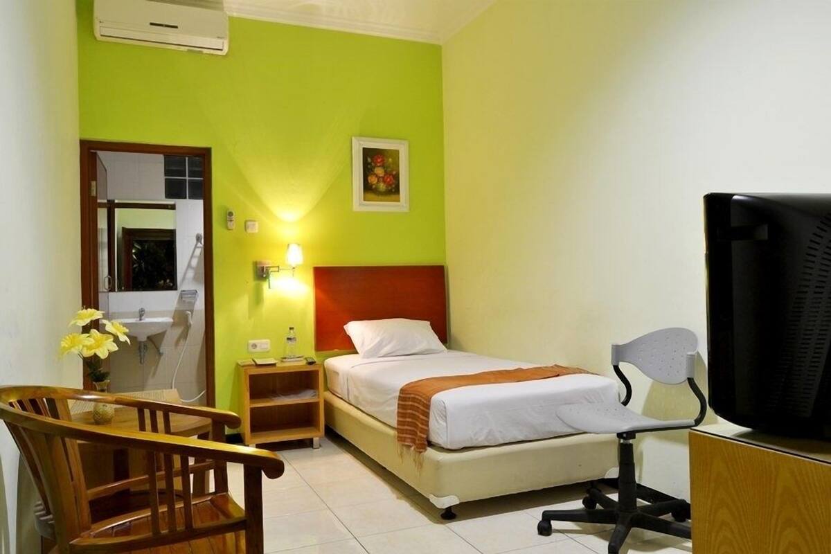 A hotel room with a bed, a desk, a chair, a TV, and a bathroom visible through an open door.