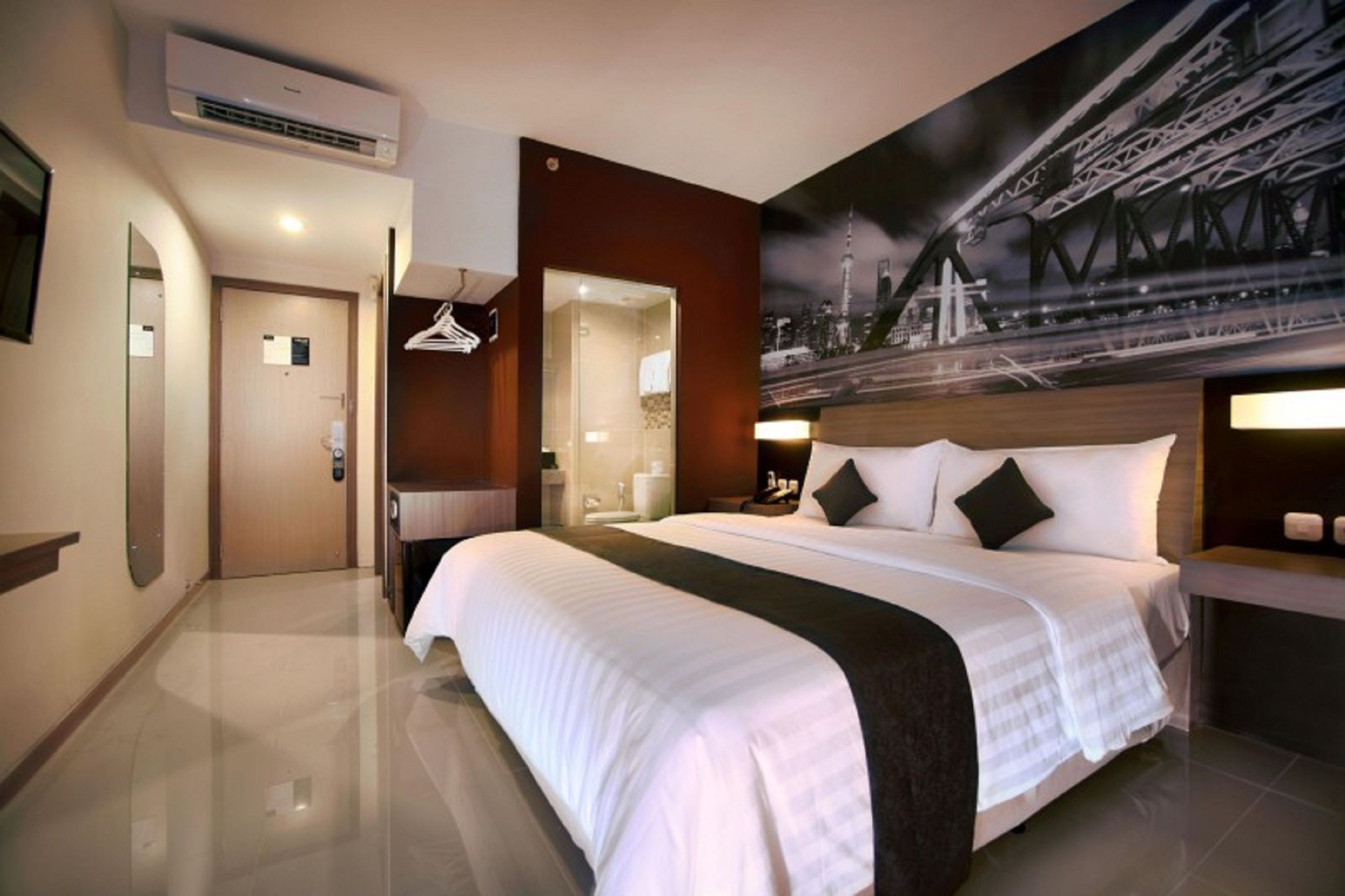 A hotel room with a large bed, a bathroom, a wardrobe, and a cityscape mural on the wall.