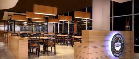 A modern restaurant interior with a wooden reception desk, multiple seating areas, and pendant lighting.