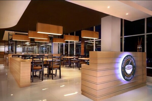 A modern restaurant interior with a wooden reception desk, multiple seating areas, and pendant lighting.