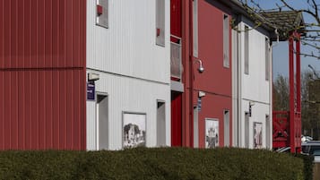 En röd och vit byggnad med ett platt tak, en liten balkong och en häck framför.