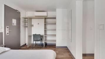 A modern hotel room with a bed, a desk, and a built-in wardrobe.