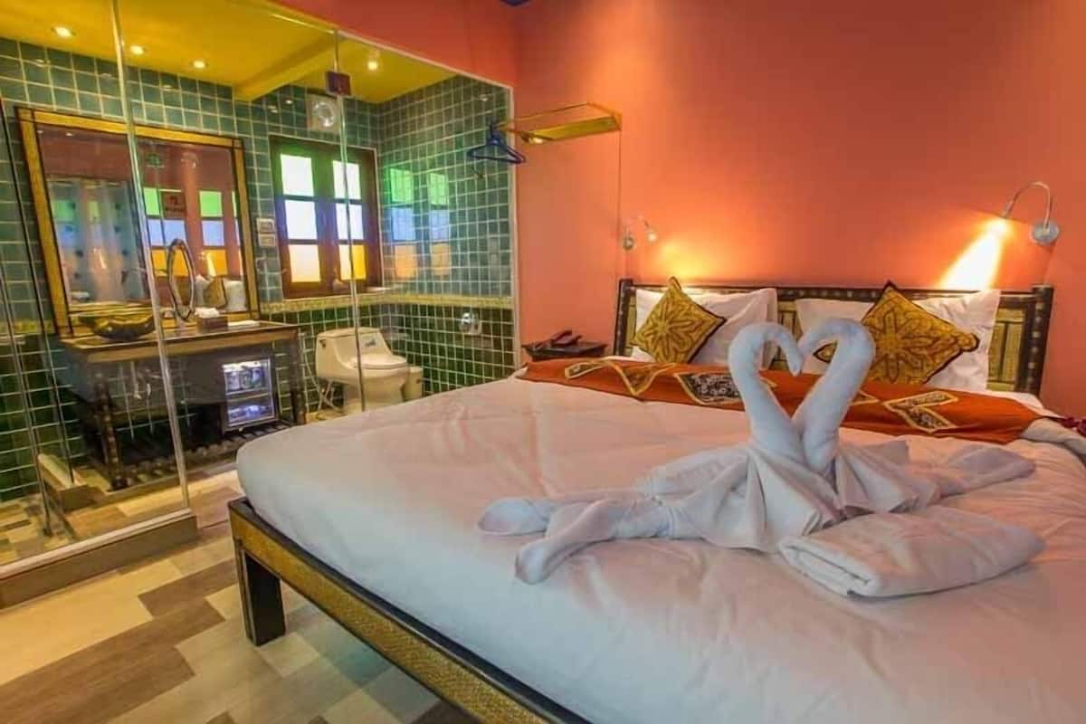A hotel room with a bed, a glass shower enclosure, and a mirror.