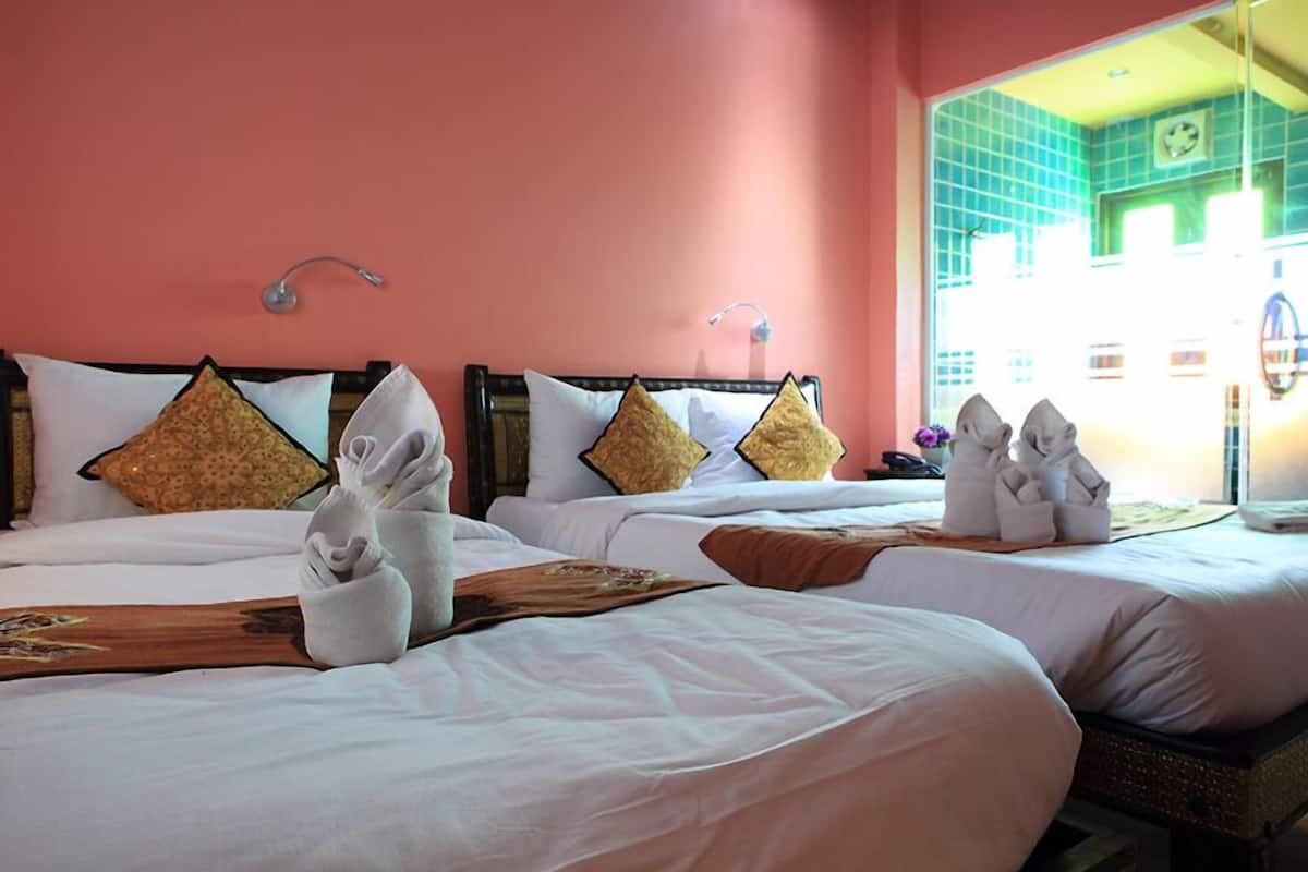 A hotel room with two beds, each with white linens and decorative pillows. There are towels neatly arranged on the beds.