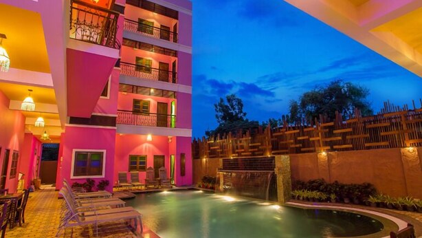 Un hotel de varios pisos con zona de piscina, mobiliario exterior y una cascada.