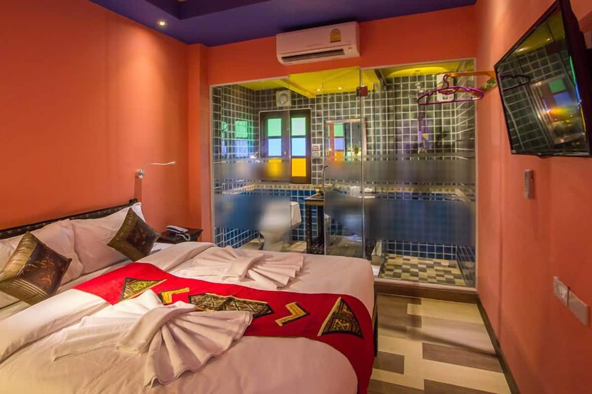 A hotel room with a bed, a bathroom with a glass door, and a TV mounted on the wall.
