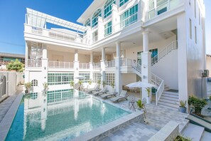 A multi-story building with a swimming pool, outdoor seating, and a staircase.