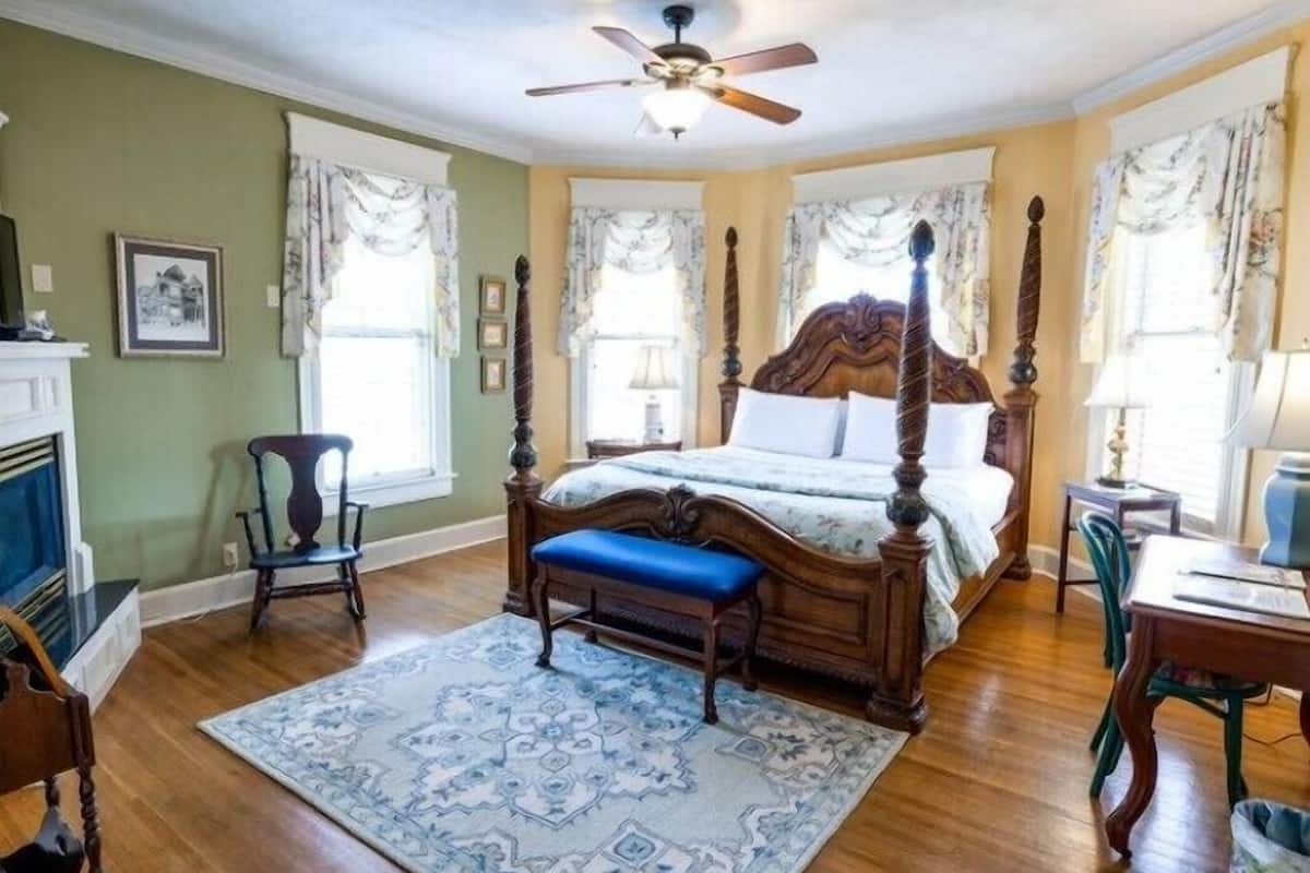 A bedroom with a four-poster bed, a wooden bench, a desk, and a chair.