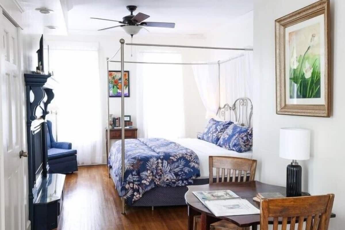 A bedroom with a four-poster bed, a ceiling fan, a desk with a chair, and a table with a lamp.