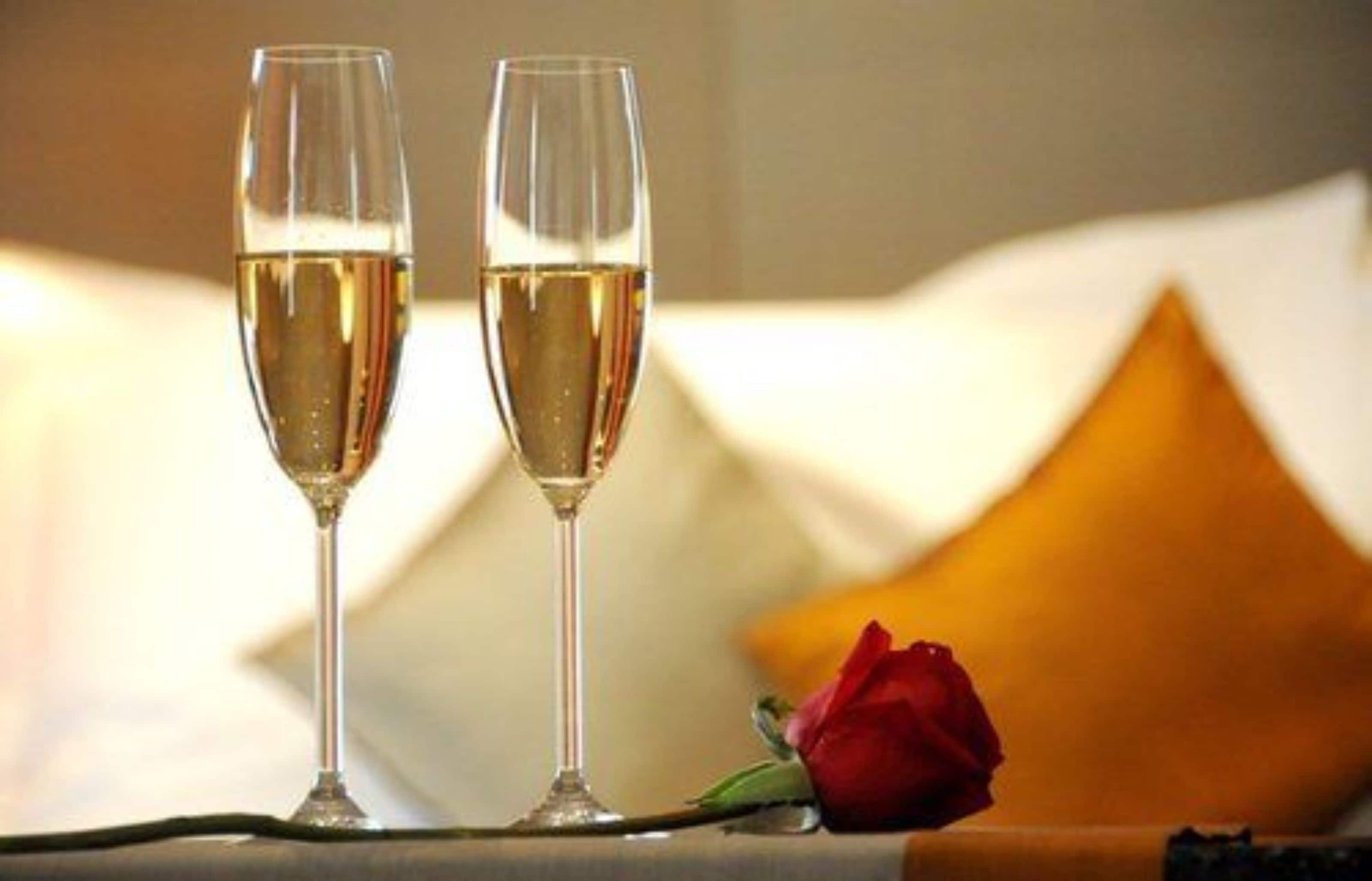 Twee champagneglazen op een tafel met een enkele roos ernaast.