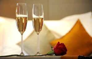 Two champagne flutes on a table with a single rose beside them.