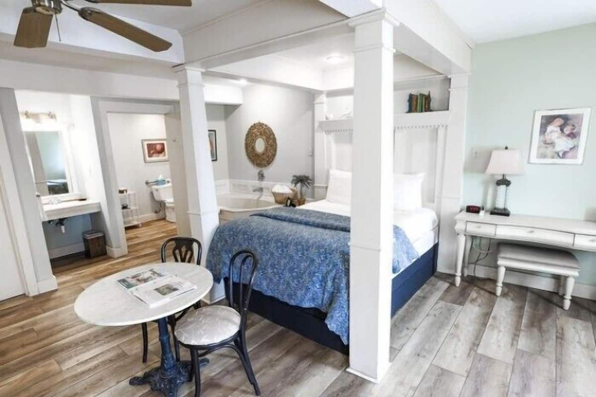 A room with a bed, a desk, a chair, a round table, and a ceiling fan.