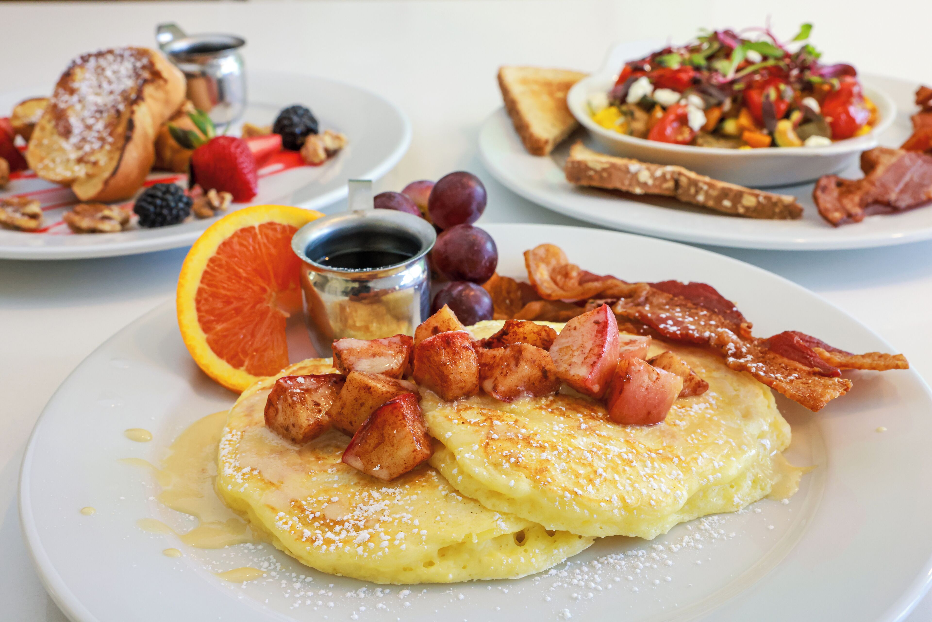 Un plato de desayuno con tortitas, tocino y fruta.