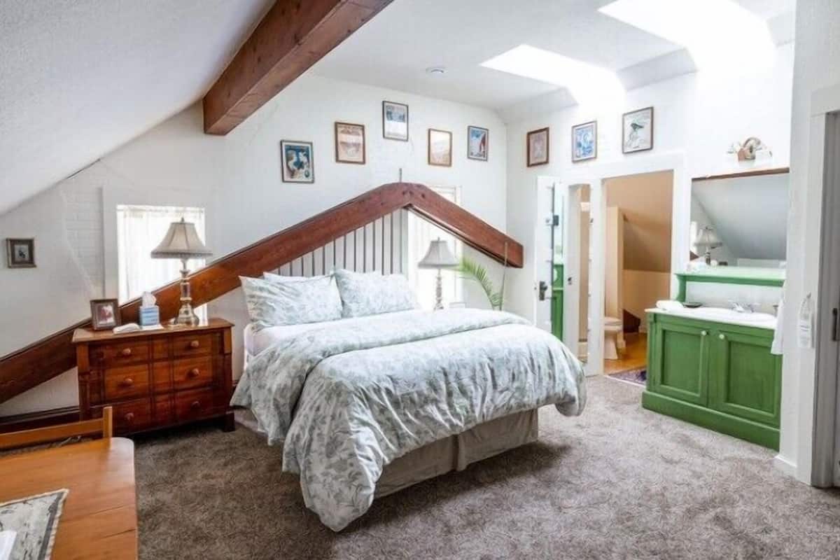 A bedroom with a sloped ceiling, a bed with a grey duvet, a wooden dresser, and a green cabinet.