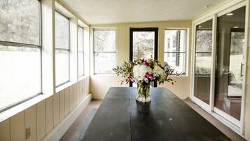 Um quarto com uma mesa de madeira escura, um vaso com flores e janelas grandes com vista para árvores.