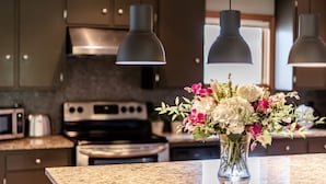 Une cuisine avec des meubles de couleur sombre, une cuisinière en acier inoxydable et des luminaires suspendus.