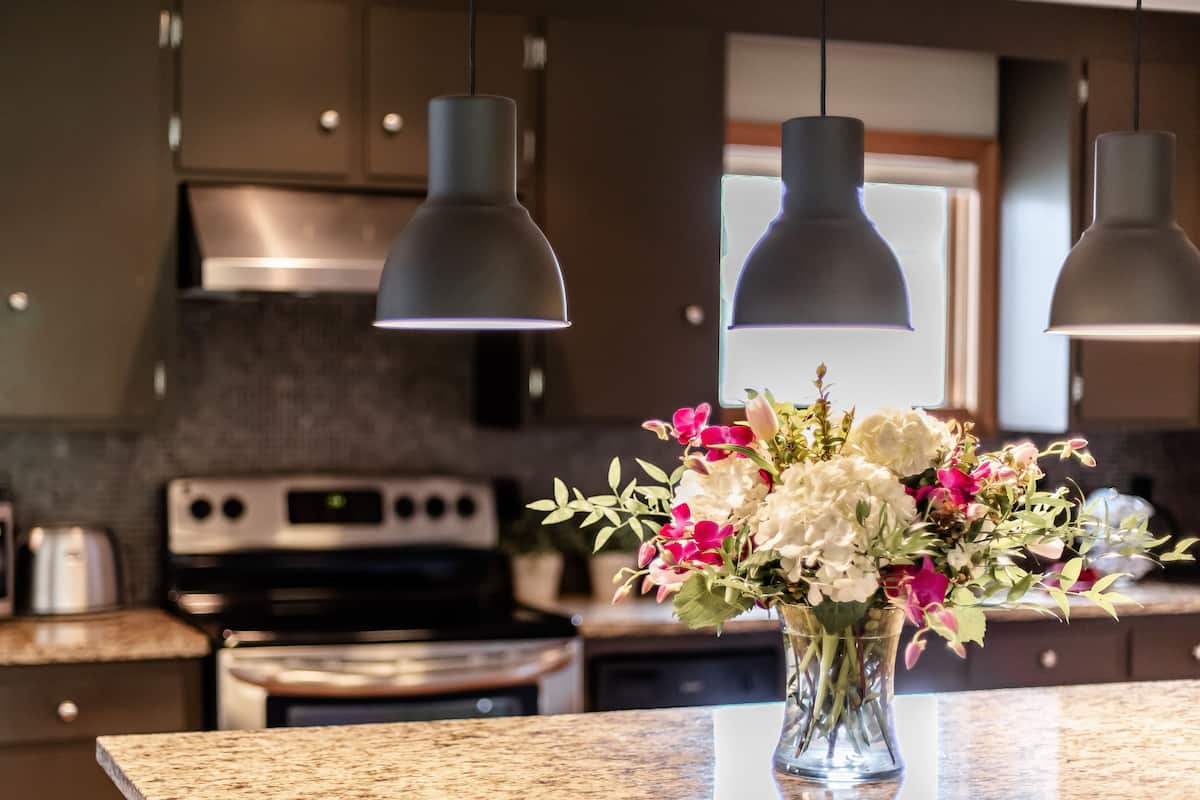 Une cuisine avec des meubles de couleur sombre, une cuisinière en acier inoxydable et des luminaires suspendus.